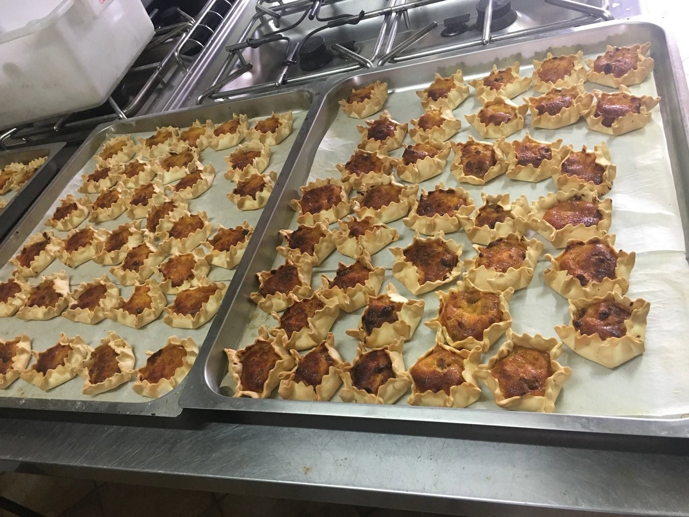 Tortine a stella con bordo pizzicato e ripieno dorato su teglie d'acciaio nella cucina dell'Agriturismo Monte Alma